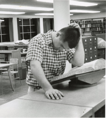 Photograph of a student in the 1950s looking up something in a dictionary. 